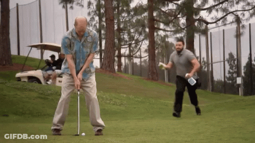 A Man In A Hawaiian Shirt Is Swinging A Golf Club On A Golf Course GIF