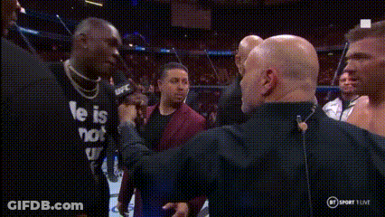 A Man In A He Is Not Shirt Is Talking Into A Microphone While Another Man Looks On . GIF