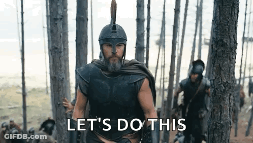 A Man In A Helmet And Armor Is Walking Through A Forest With A Group Of Soldiers . GIF