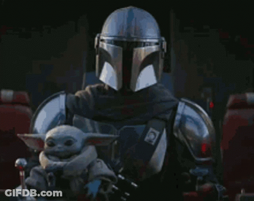 A Man In A Helmet Is Holding A Baby Yoda In His Lap . GIF