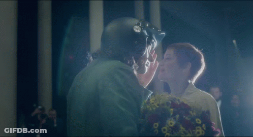 A Man In A Helmet Kisses A Woman With Flowers GIF
