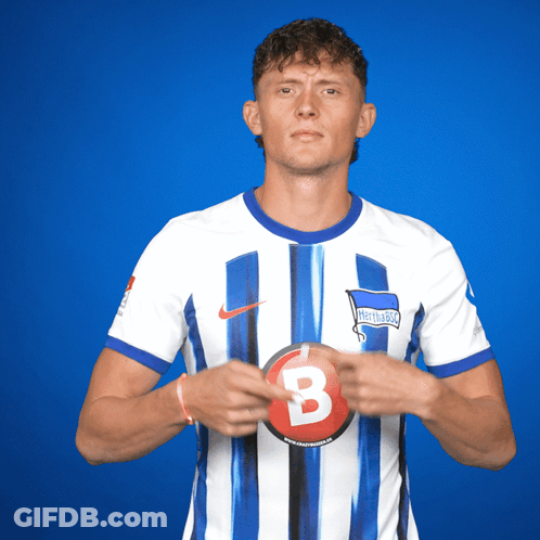 A Man In A Hertha Berlin Jersey Holds A Red B GIF