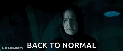 A Man In A Hood Is Holding A Glass And Says `` Back To Normal '' In A Dark Room . GIF