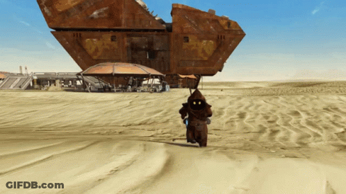 A Man In A Hood Is Walking In The Sand Near A Large Building GIF
