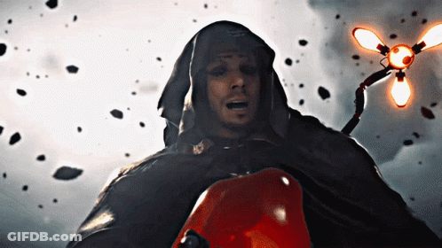 A Man In A Hooded Cape Holds A Red Object In His Hand GIF