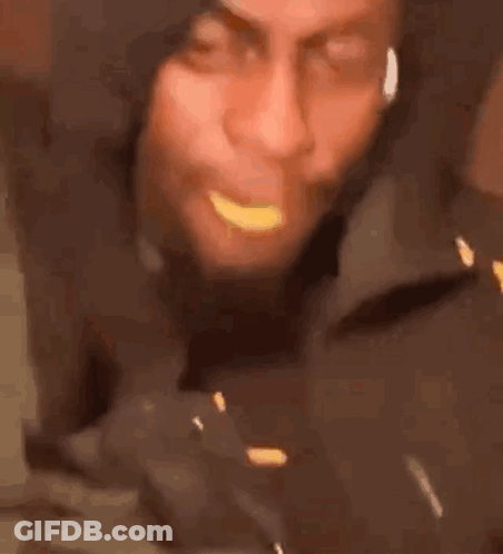 A Man In A Hooded Jacket Is Eating A Piece Of Food . GIF
