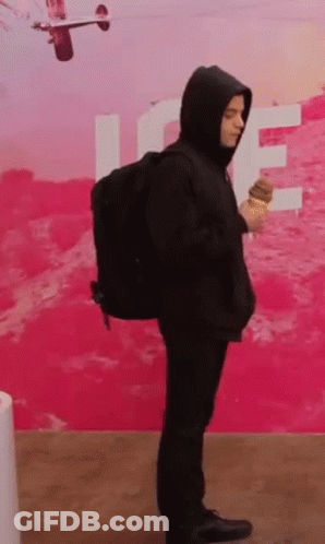 A Man In A Hooded Jacket Is Holding An Ice Cream Cone . GIF