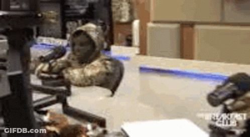 A Man In A Hooded Jacket Is Sitting In Front Of A Microphone In A Room . GIF
