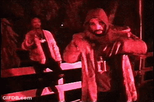 A Man In A Hooded Jacket Is Standing In A Dark Room Holding A Bag . GIF