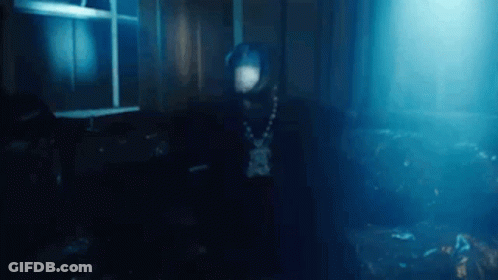 A Man In A Hooded Jacket Is Standing In A Dark Room . GIF