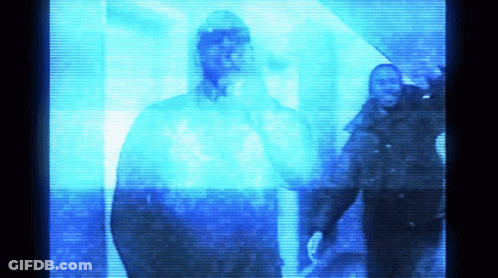 A Man In A Hooded Jacket Is Standing In A Dark Room GIF