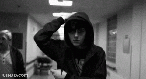 A Man In A Hooded Jacket Is Standing In A Hallway . GIF