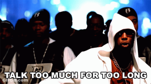 A Man In A Hooded Jacket Stands In Front Of A Crowd With The Words " Talk Too Much For Too Long " Below Him GIF