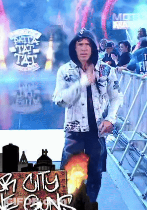 A Man In A Hooded Jacket Stands In Front Of A Sign That Says City Of Guns GIF