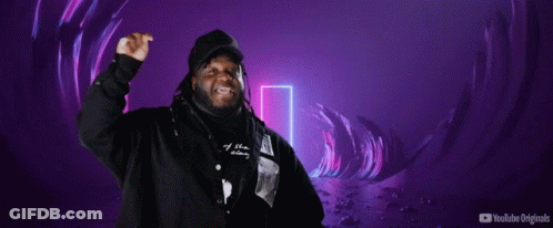 A Man In A Hooded Jacket Stands In Front Of A Sign That Says Mi Escena Musical GIF