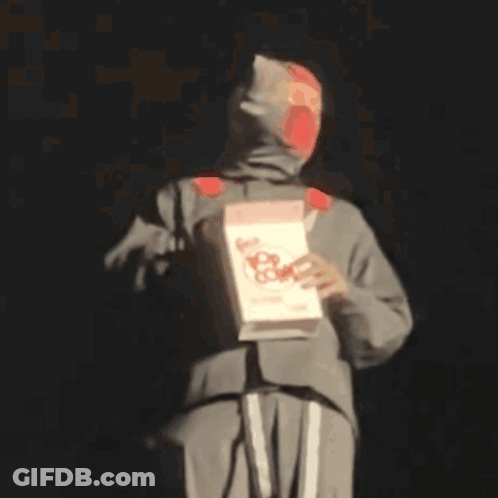 A Man In A Hooded Sweatshirt Is Holding A Box Of Nacho Cheese .. GIF