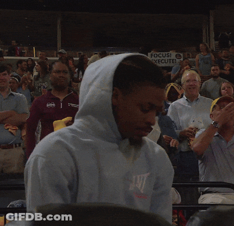 A Man In A Hooded Sweatshirt Stands In Front Of A Sign That Says Focus Execute GIF