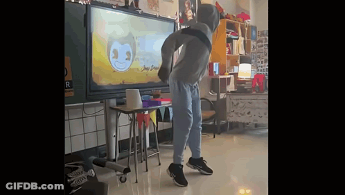 A Man In A Hoodie Is Dancing In A Classroom In Front Of A Large Screen . GIF