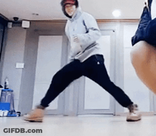A Man In A Hoodie Is Dancing In A Room With A Woman Standing Behind Him . GIF