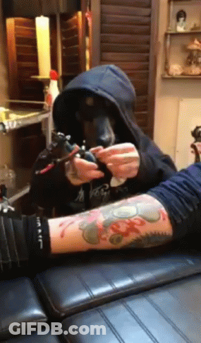 A Man In A Hoodie Is Getting A Tattoo On Another Man 'S Arm GIF