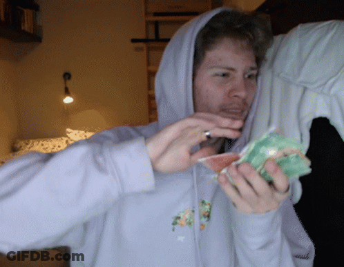 A Man In A Hoodie Is Holding A Piece Of Fruit In His Hands GIF