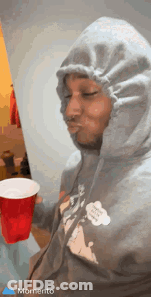 A Man In A Hoodie Is Holding A Red Cup In His Hand . GIF