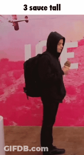 A Man In A Hoodie Is Holding An Ice Cream Cone In Front Of A Pink Wall With The Words 3 Sauce Tall Above Him GIF