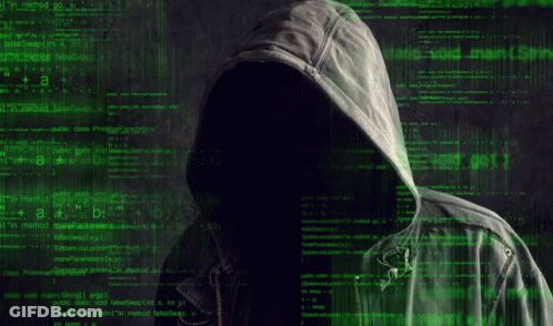 A Man In A Hoodie Is Sitting At A Table With A Laptop Computer . GIF