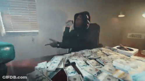 A Man In A Hoodie Is Sitting At A Table With A Pile Of Money On It . GIF