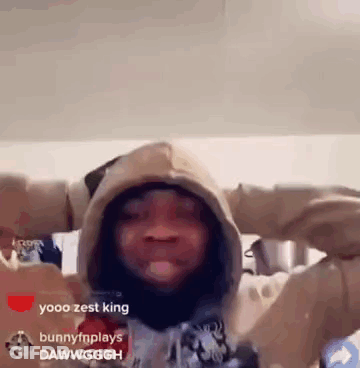A Man In A Hoodie Is Standing In A Room With His Arms Outstretched And Looking At The Camera . GIF