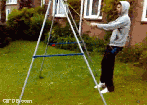 A Man In A Hoodie Is Standing In Front Of A Swing Set In A Yard GIF