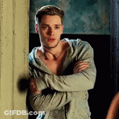 A Man In A Hoodie Is Standing Next To A Wall With His Arms Crossed And Looking At The Camera . GIF