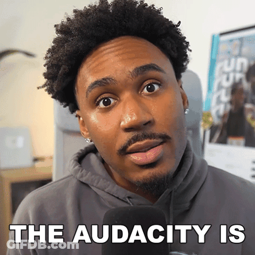 A Man In A Hoodie Is Talking Into A Microphone With The Words " The Audacity Is " Behind Him GIF