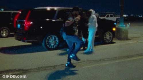 A Man In A Hoodie Stands In Front Of A Black Suv GIF