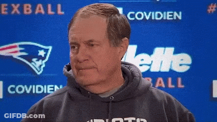 A Man In A Hoodie Stands In Front Of A Screen That Says Exball Covidien And Gillette GIF