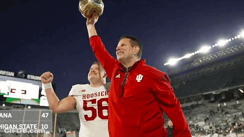 A Man In A Hoosier 56 Jersey Holds Up A Football GIF