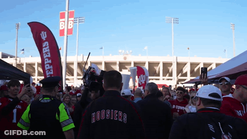 A Man In A Hoosier 'S Jacket Stands In Front Of A Crowd GIF