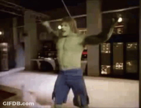 A Man In A Hulk Costume Is Standing In A Room With His Arms Outstretched And Holding A Stick . GIF