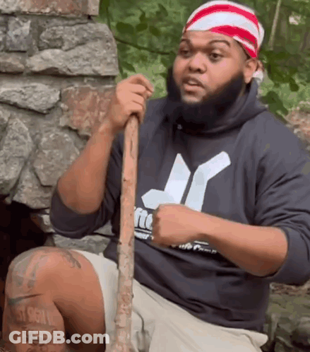 A Man In A Hurley Sweatshirt Holds A Wooden Stick GIF