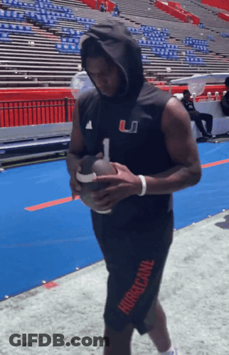 A Man In A Hurricane Shorts Holds A Football In His Hands GIF