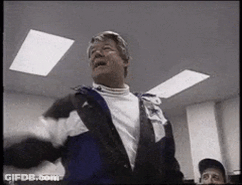 A Man In A Jacket Is Standing In A Room With A Man In A Baseball Cap . GIF