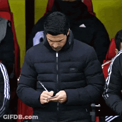 A Man In A Jacket Is Writing On A Piece Of Paper With A Pen . GIF