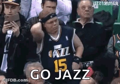 A Man In A Jazz Jersey Is Sitting In The Stands Watching A Basketball Game And Says `` Go Jazz '' . GIF