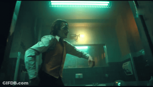 A Man In A Joker Costume Is Standing In A Dark Room GIF