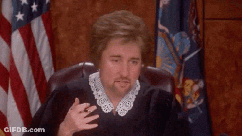 A Man In A Judge 'S Robe Is Sitting In Front Of A Flag . GIF