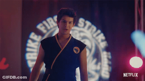 A Man In A Karate Uniform Is Standing In Front Of A Sign That Says Strike Fire Strike . GIF