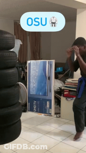 A Man In A Karate Uniform Is Standing In Front Of A Stack Of Tires And A Samsung Tv GIF