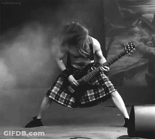 A Man In A Kilt Is Playing A Guitar In A Black And White Photo GIF