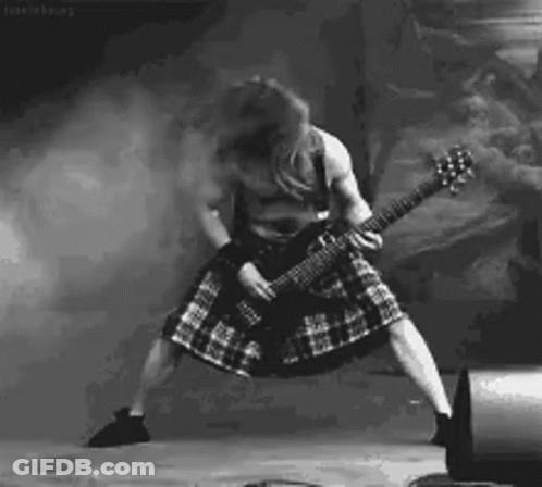 A Man In A Kilt Is Playing A Guitar On Stage In A Black And White Photo . GIF