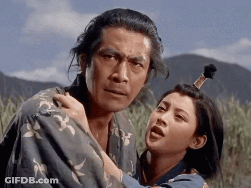 A Man In A Kimono Is Holding A Woman In A Field With Mountains In The Background GIF